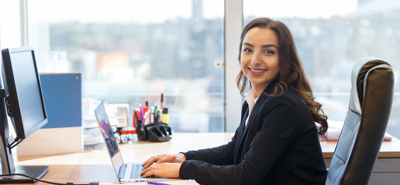 Vrouw zittend aan bureau, kijkt in camera.