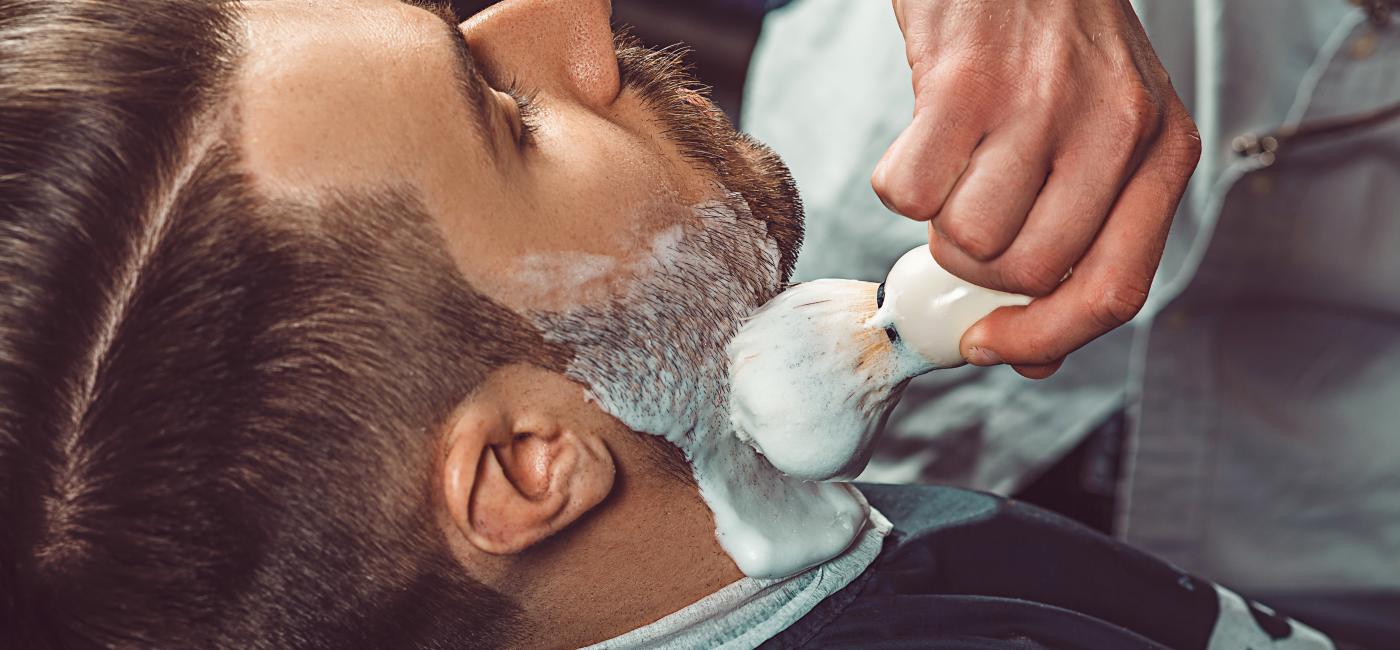 Kin van man in kappersstoel wordt ingezeept door barbier