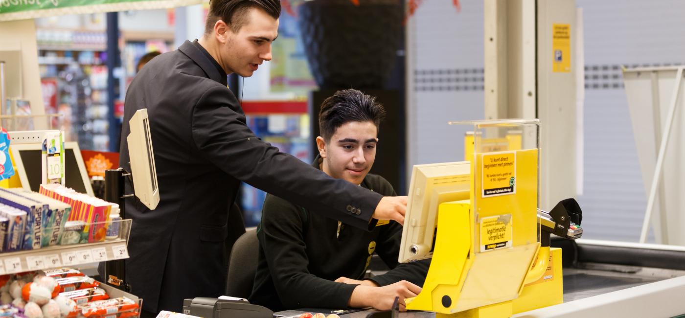 Man geeft uitleg aan mannelijke kassier in winkel.