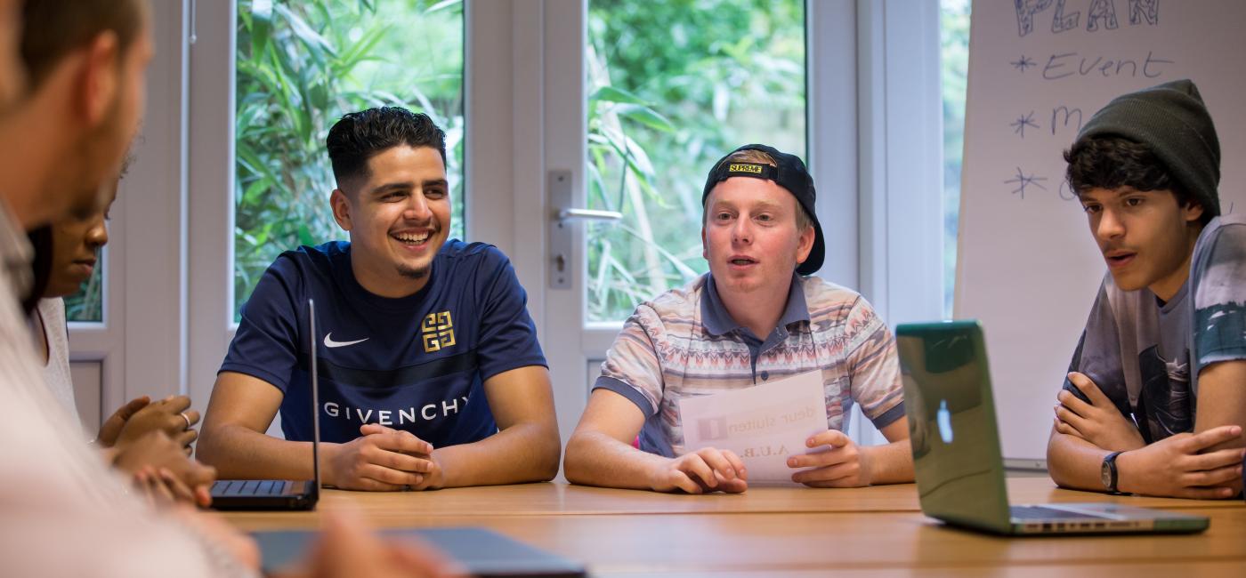 Een docent en vier studenten aan een tafel