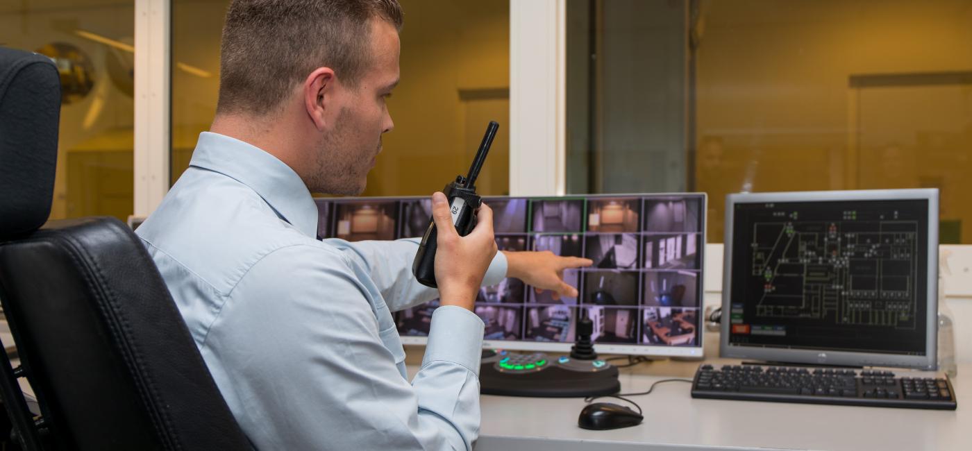 Beveiliger met portofoon in handkijkt naar cctv scherm