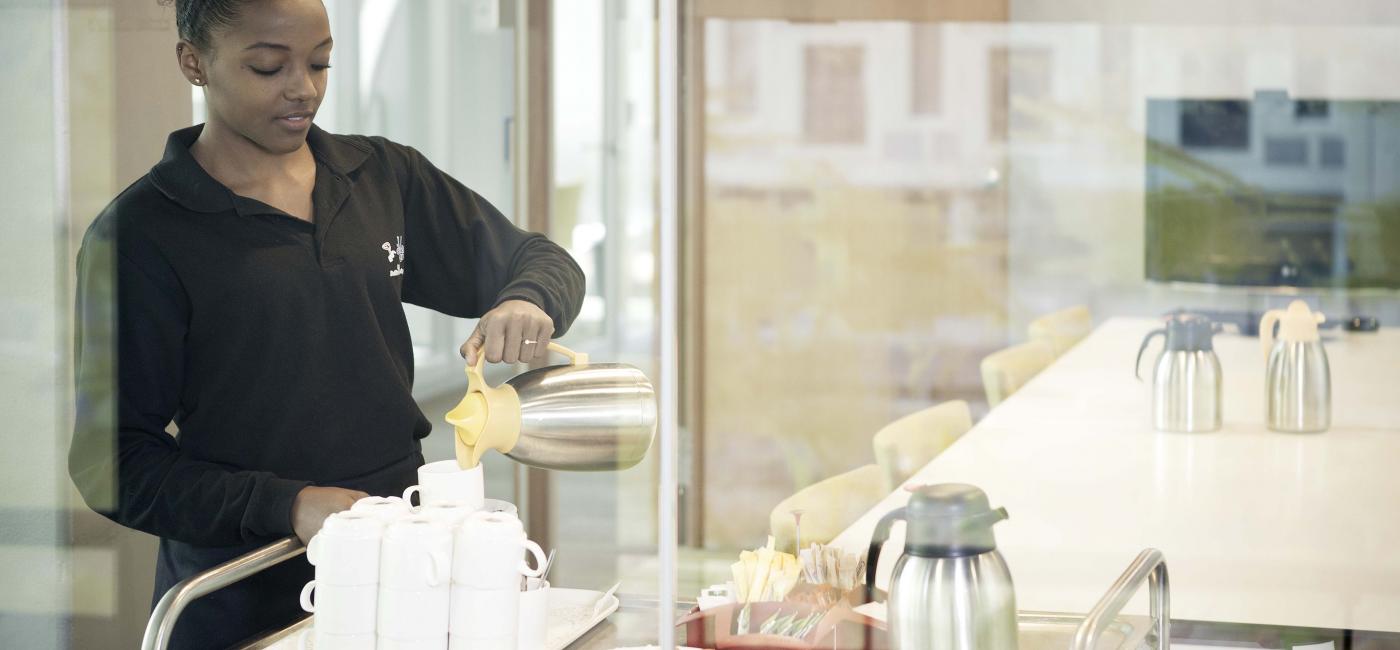 Jonge vrouw schenkt koffie uit een kan in een kopje