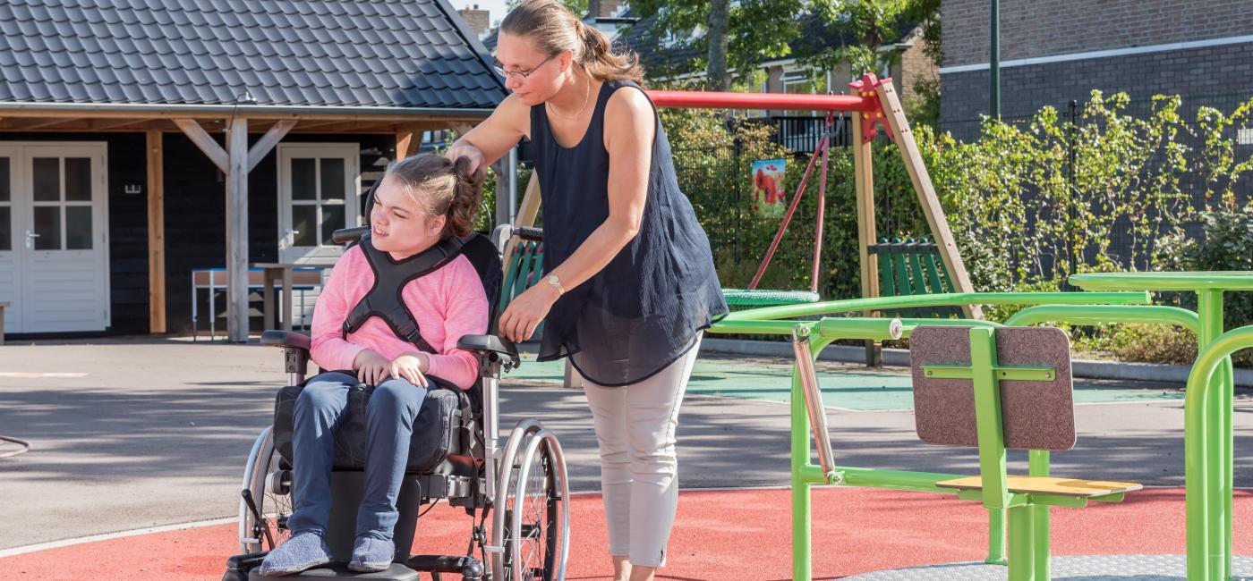 Begeleider duwt rolstoel met gehandicapt meisje