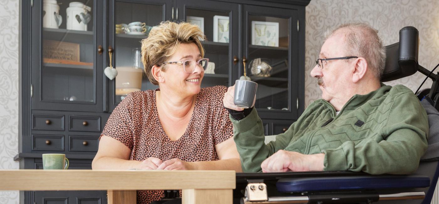 Vrouw zit aan tafel met man in rolstoel